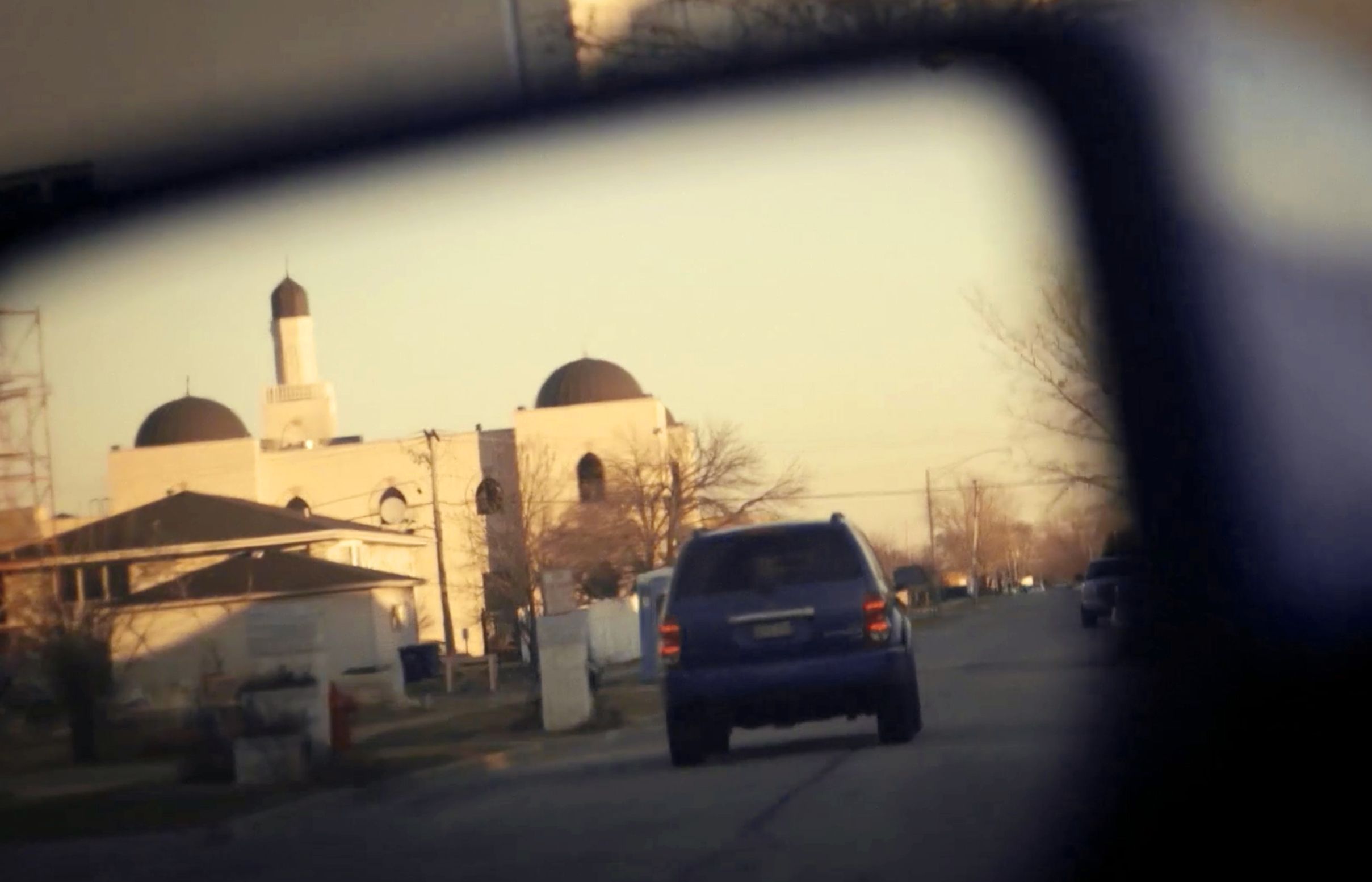 a small photo of a rearview mirror, where in the background, a masjid and a black car